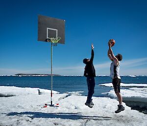 Two men play basketball on ice