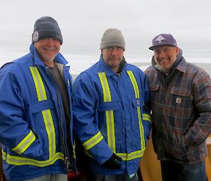 There plumbers (middle man pulling a funny face) standing on the Aurora Australis with water and sea ice in the background.