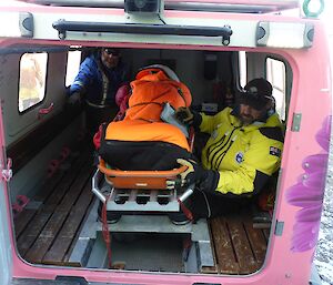 The pink Hägglunds painted in support of Breast Screen Australia backs carefully toward the medical clinic receiving area with the stretcher and two expeditioners in the rear cab.