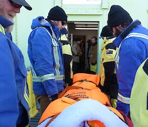 Expeditioners stand opposite each in a long line to receive the stretcher as it is passed hand to hand through a cold porch entry.