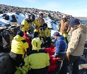 Seven Expos dressed in either yellow and black gortex shell or padded carhartt jackets provide care to the patient.