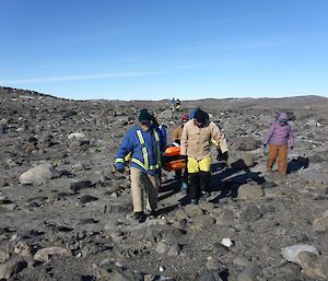 Six expeditioner on the stretcher team, an additional guide to get through the rocky ground on the clear blue sky Davis afternoon.