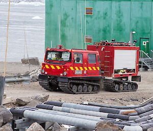 The bright red fire hagglunds vehicle driving up the hill towards the summer accommodation building.