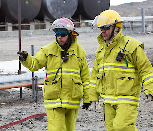 Two fire crew members dressed in full firefighting turnout protective clothing discussion the situation at hand.