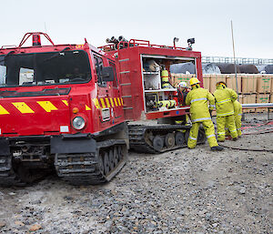 The bright red fire hagglunds park on scene with three fire team members at the rear of the vehicle setting up the fire hose.