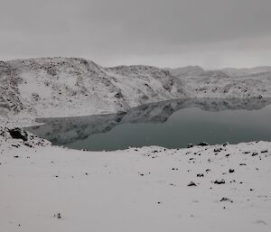 Snowy hills and reflection in calm lake waters.