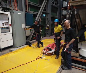 Three smiling expeditioners standing around a stretcher that is on the ground.