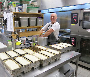 The chef standing behind the full bread tins that are ready to go into the oven.