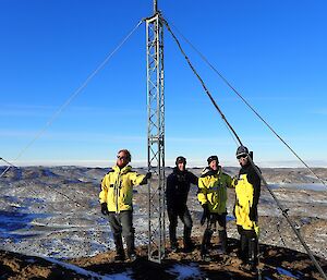 Four expeditioners standing around the repeater mast on top of Tarbuck with magnificent 360° views of the lightly snow covered Vestfold Hills.