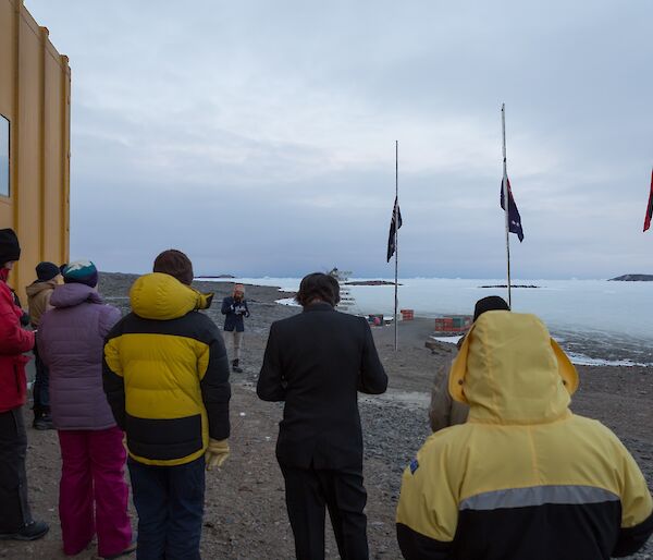 Expeditioners conducting the Anzac dawn service at the station flagpoles with the Australian, aboriginal and New Zealand flags at half-mast.