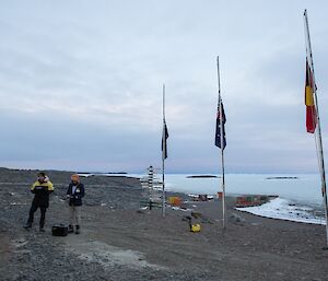 Expeditioner reads the Ode of Remembrance with the three flags at half-mast to the right and the endless sea ice in the background.