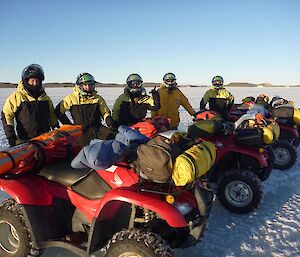 A Line up of Quad bikes with expeditioners standing behind them on the sea ice under clear blue skies.