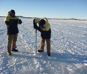 Expeditioners drilling sea ice to test for thickness with a long one metre ice drill.