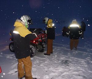 Expeditioners preparing for a quad trip on a dark and snowy morning, the reflective material on outer garments illuminated.