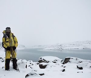 Two expeditioners dressed in yellow wind proof clothing with the snow covered hills and Deep Lake in the background.