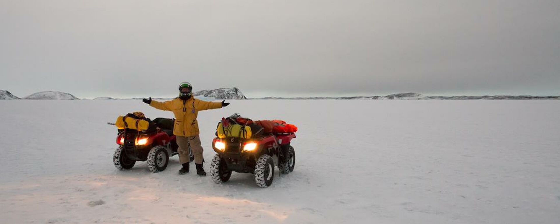 Daniel standing with two Quad bikes before sunrise on the sea ice with shore in the distance