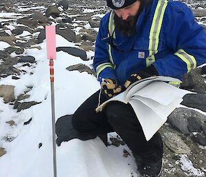 Trevor crouching down next to bore hole writing down data results