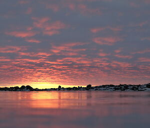 An image of a glowing sunrise reflected in the freshwater ice lake.