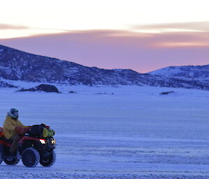 An image of the sunset with a quad bike rider coming in from the field across the sea ice.