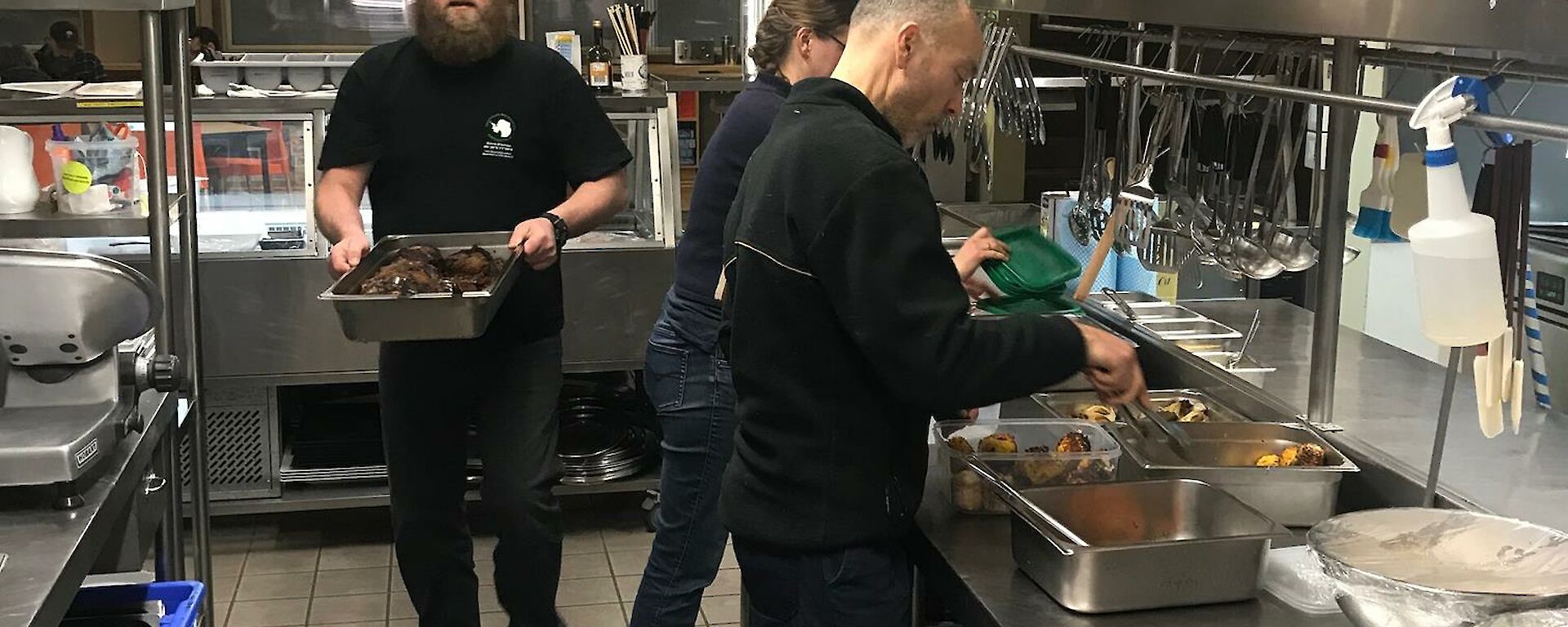 Three expeditioners in the kitchen helping the slushy put the food away after the evening meal.