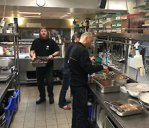 Three expeditioners in the kitchen helping the slushy put the food away after the evening meal.