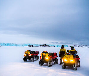 Three quad biked with head lights on in the foreground and the massive blue coloured Sørsdal glacier in the background.