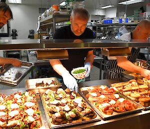 The station chef on the right with two helpers putting the final toppings on food under the warming lights.