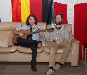 Two expeditioners sitting on the couch as one tunes his guitar.