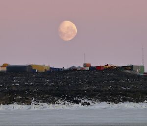 A photo of the near-full-moon setting over the buildings of Davis, looking south.