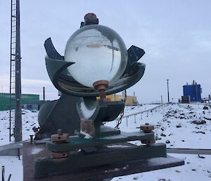 Glass globe used for measuring sunlight hours with buildings and snow covered rocks in background.