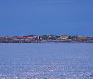 Coloured buildings in snow and rock landscape with moon rising over hills in background