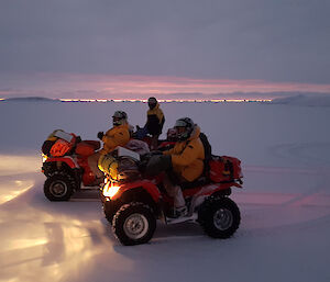 Glen, Simon and Derryn on quad bikes with their headlights reflected off the sea ice, and icebergs on the horizon silhouetted by a thin band of sunset sky between the cloud and horizon.