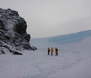 Glen, Simon and Derryn standing in the wind scour, the open space between a rocky hill on the left and a crescent-shaped wall of ice on the right.