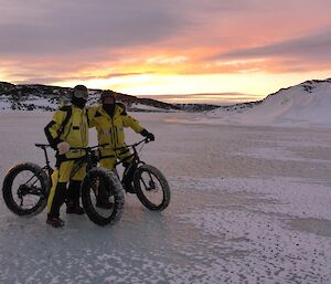 Jason and Graham stopping to pose for a photo with their bikes on the sea ice with a sunset as the backdrop.