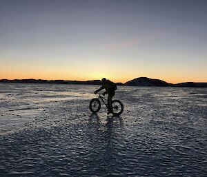 Silhouette of Jason D on his bike with an orange glow for the full length of the horizon.