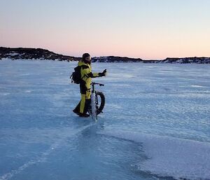 Jason D walking his bike across a section of blue snow free ice.