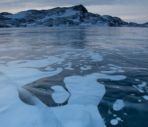 The frozen lake with patches of snow cover and the hills in the background.