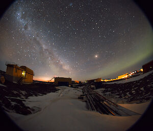 Fisheye lens used to capture an aurora on the right and the beautiful Milky Way on the left hovering over the station buildings.