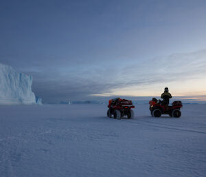 Two quad bikes on the snow covered sea ice, with large ice bergs in the background.