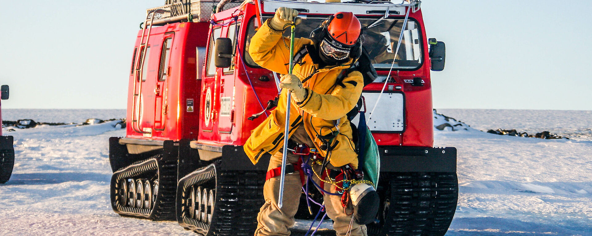 Expeditioner roped up in front of the red Hagglund vehicle probing the snow.