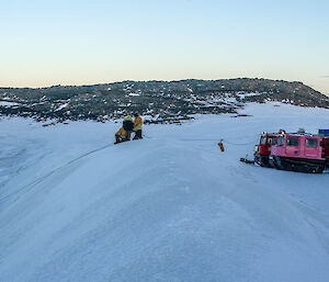 The pink Hägglunds at the edge of the ice slop with the expeditioners conducting rope rescue training.