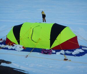 Chris taking a wind measurement with a hand held anemometer behind the fluorescent oval shaped Endurance tent.