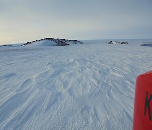 Wide open space of snow covered ice, with a couple of rocky hills in the background and the Antarctic Plateau in the distance.