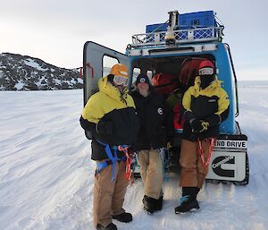 Glenn and Aaron wearing harnesses, standing at the back of the blue Hägglunds vehicle ready for crevasse probing training.