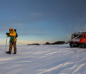 Derryn practicing probing for crevasses wielding a long metal spike while connected by a rope to the red Hägglunds vehicle.