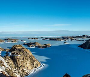 Panoramic view across the Rauer Islands from an elevated position. The hills and islands are in sunlight and the hills are casting long shadows across the sea ice between the islands.