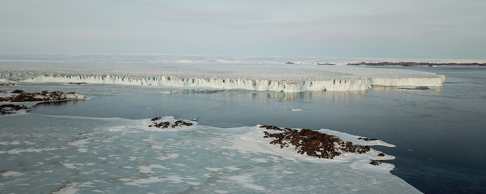 Aerial photo of the Sorsdal glacier with frozen sea ice and small rocky islands in the foreground.