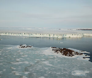 Aerial photo of the Sorsdal glacier with frozen sea ice and small rocky islands in the foreground.