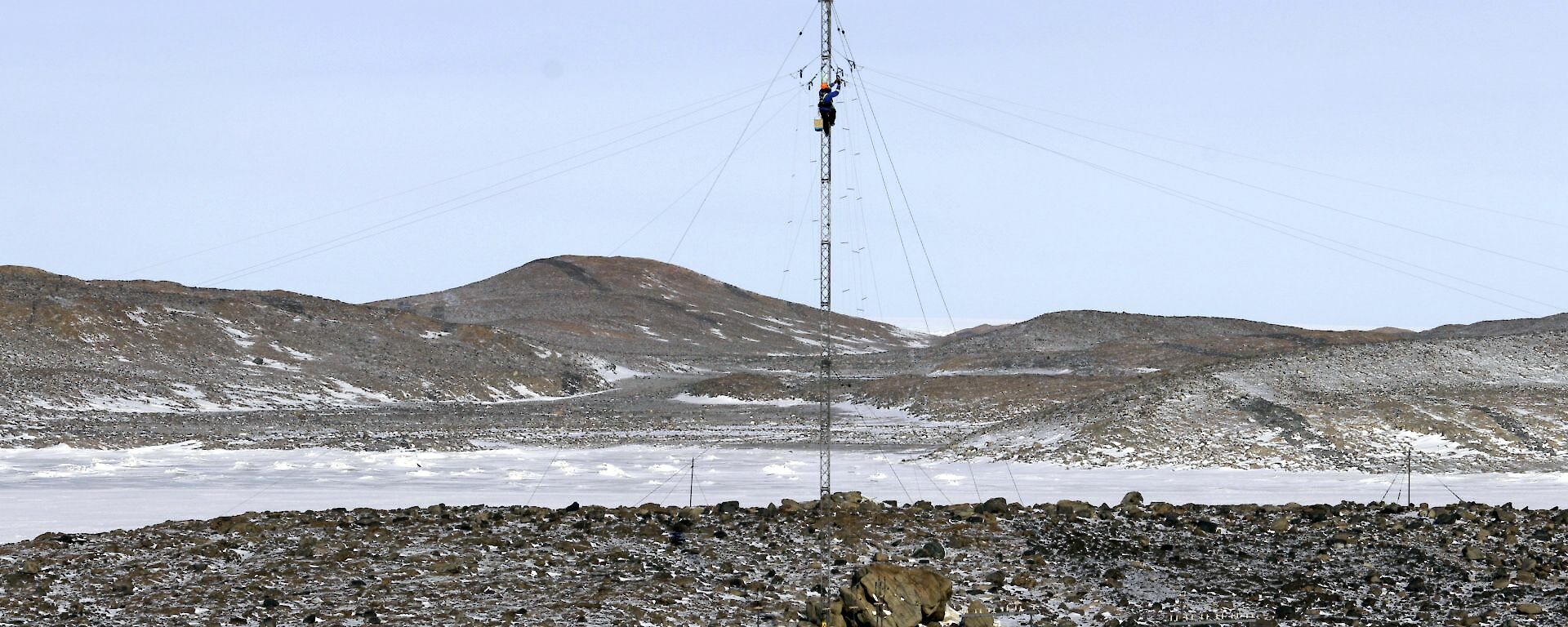 Two expeditioners on the ground looking up at the climber at the top of the mast doing the antenna repair