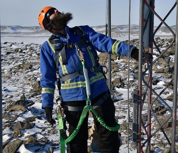 Expeditioner wearing climbing harness at the base of the mast and looking up to the top